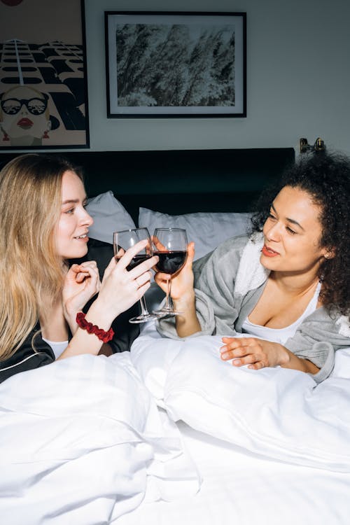 Free Two Young Women Lying on White Bed While Looking at Each Other Stock Photo