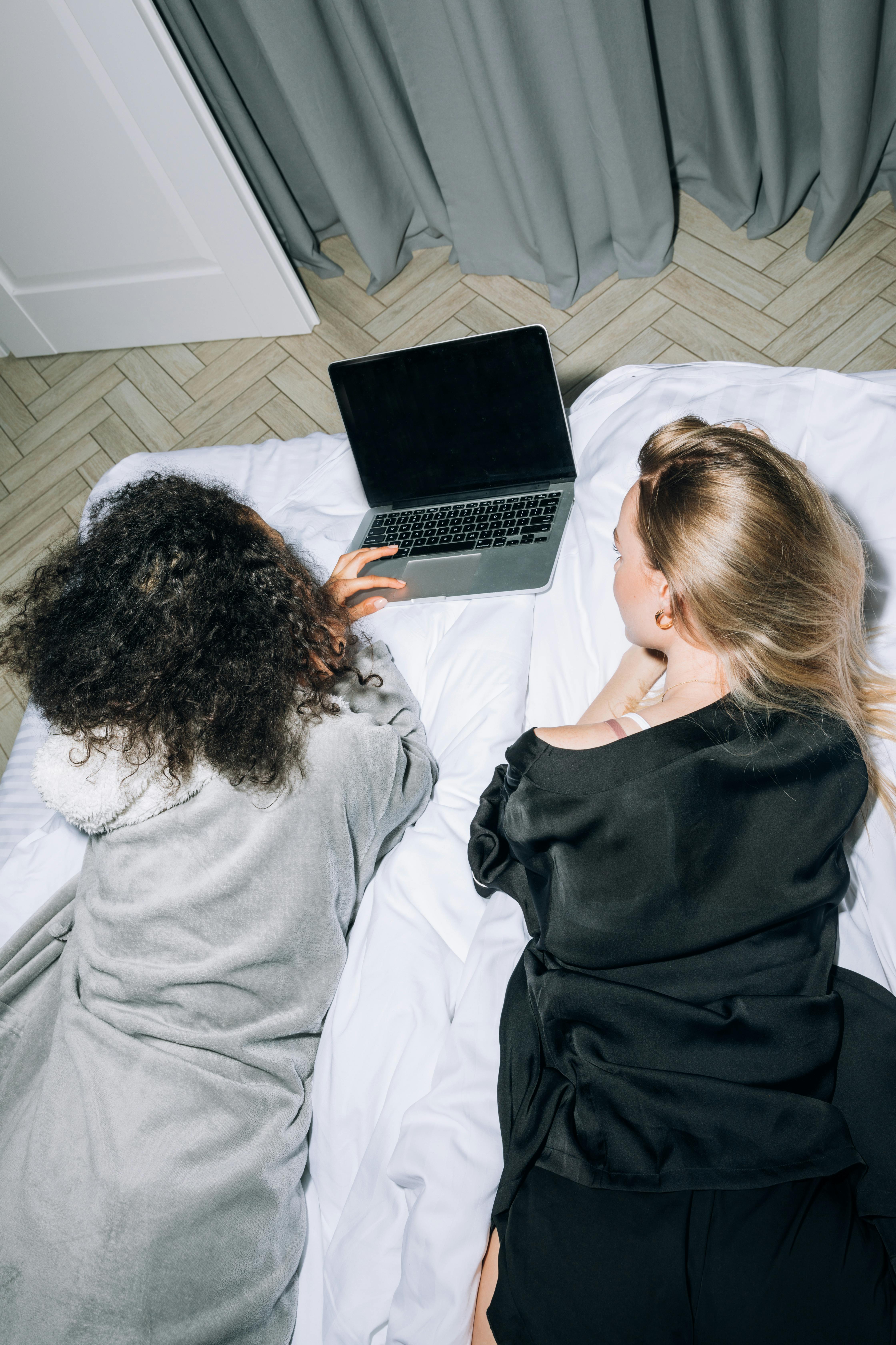 two young women lying down while looking at computer laptop