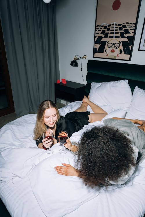 Two Women Lying Down on White Bed While Looking at Each Other