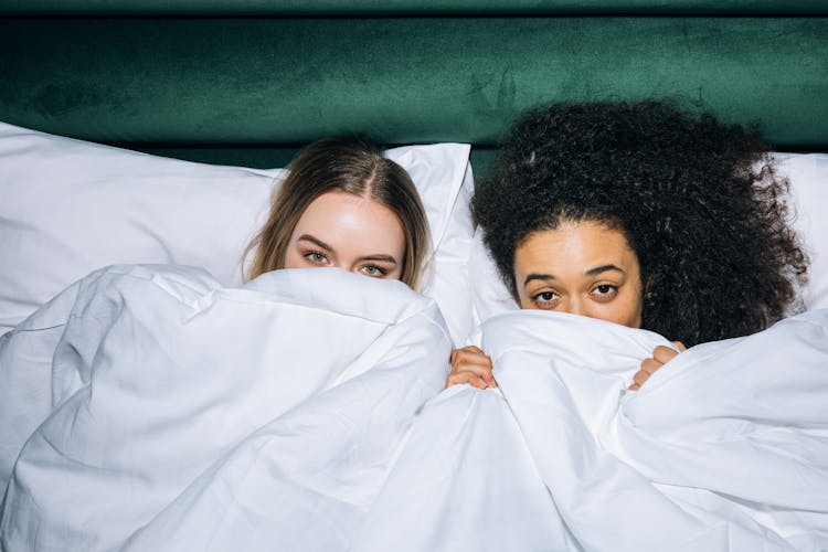 Two Young Women Lying On White Bed