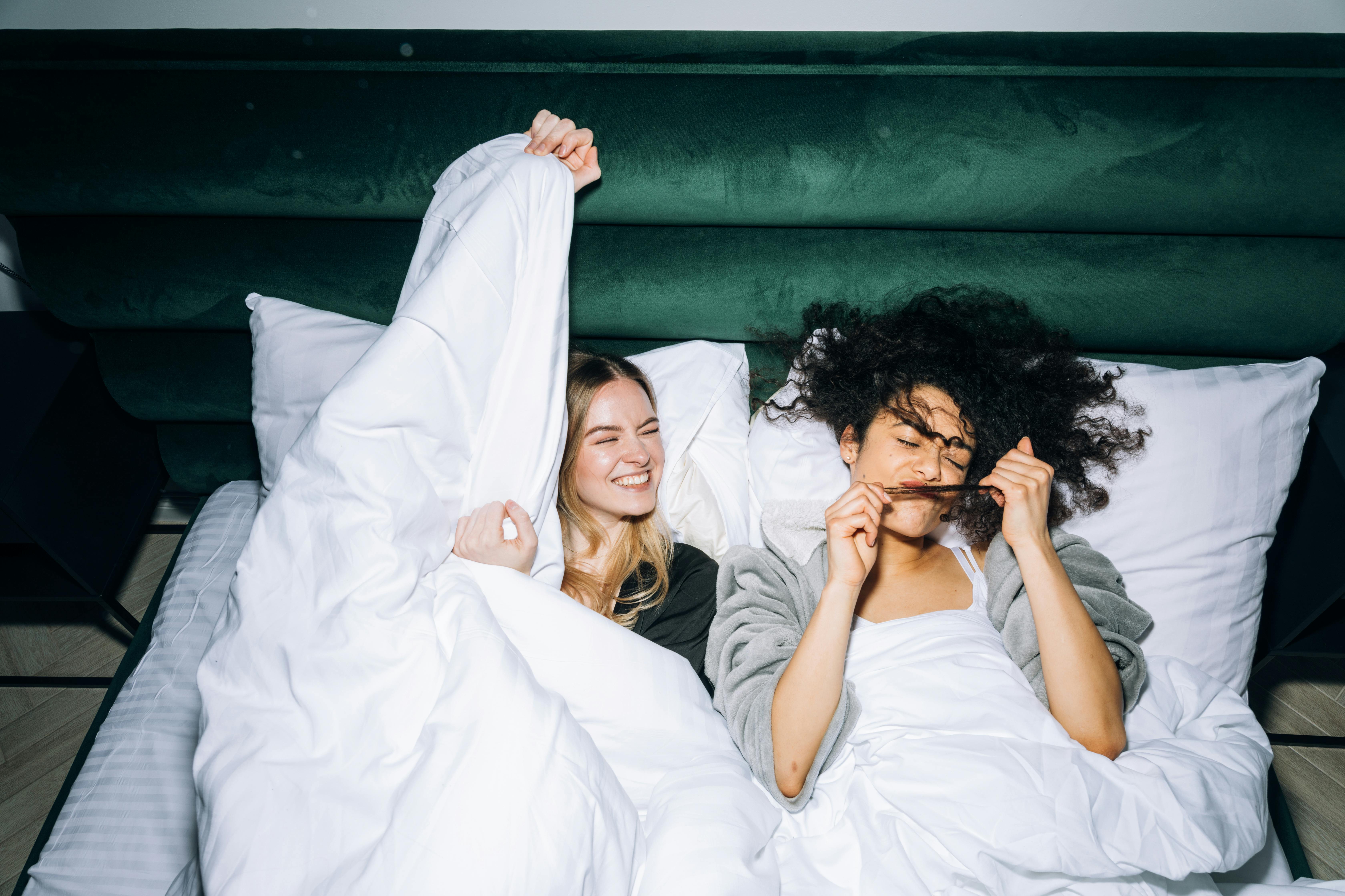 two young women having fun while lying on white bed