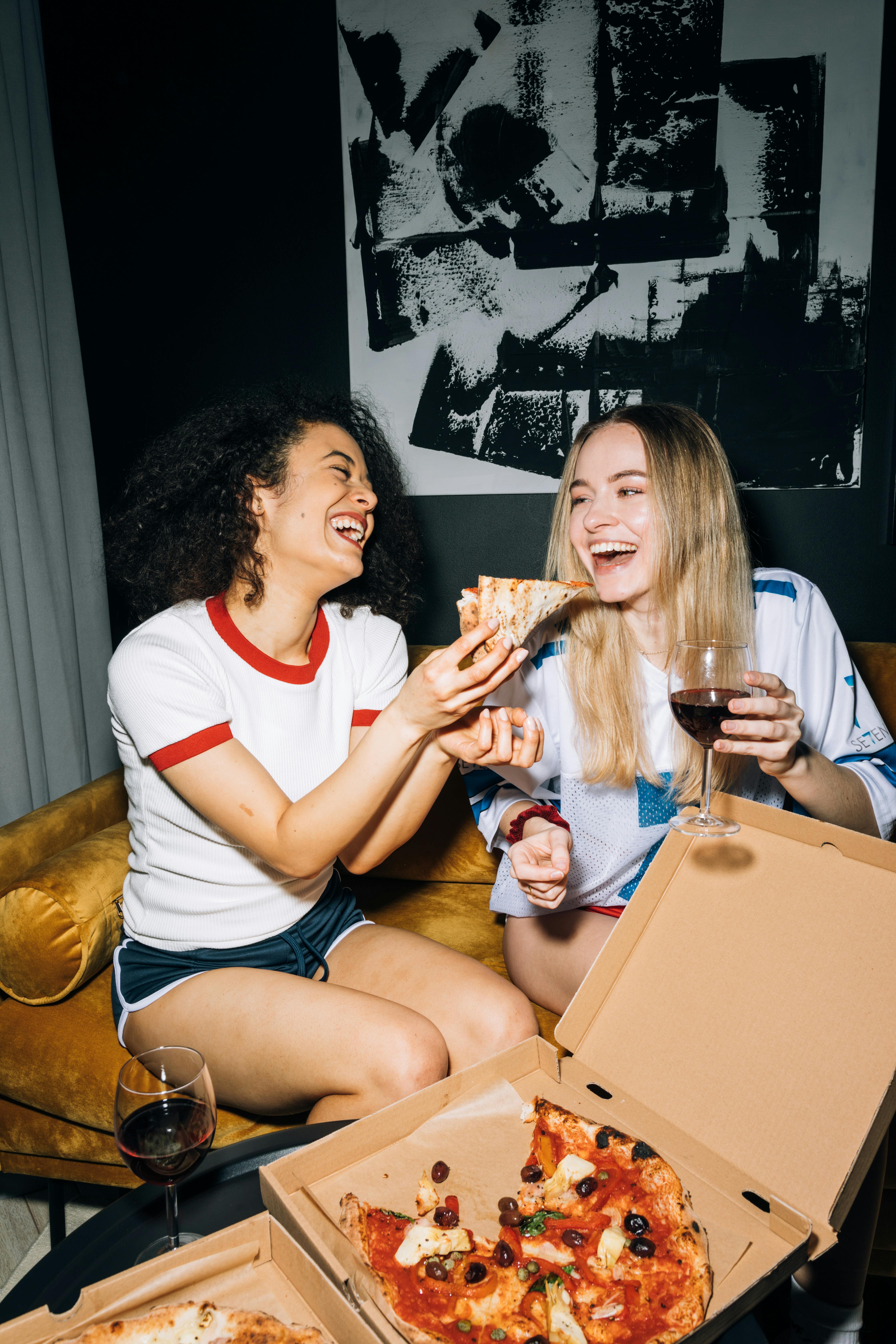 two young women having fun while eating their pizza
