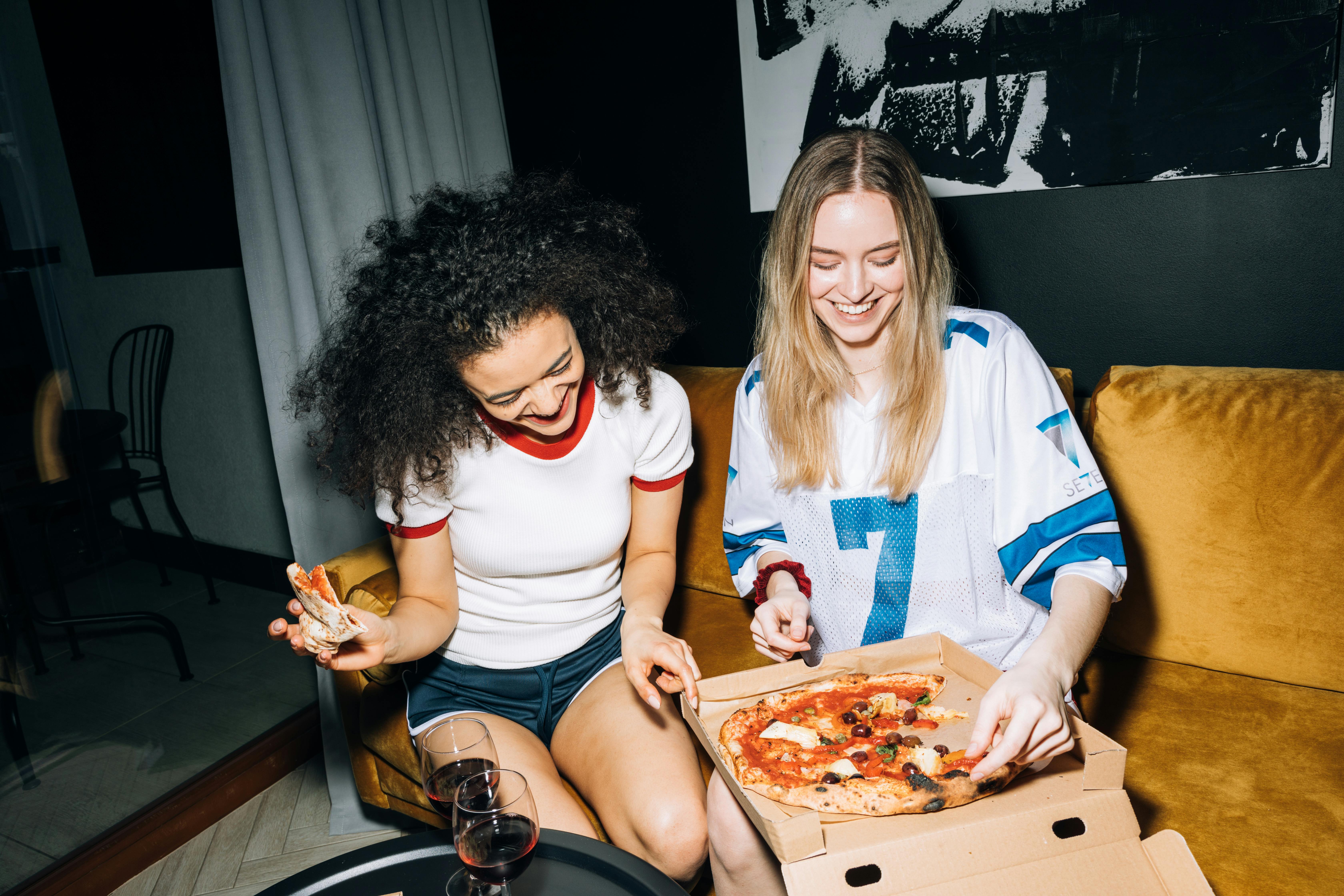 two young women eating and getting a slice of pizza