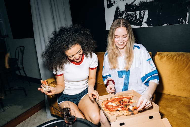 Two Young Women Eating And Getting A Slice Of Pizza