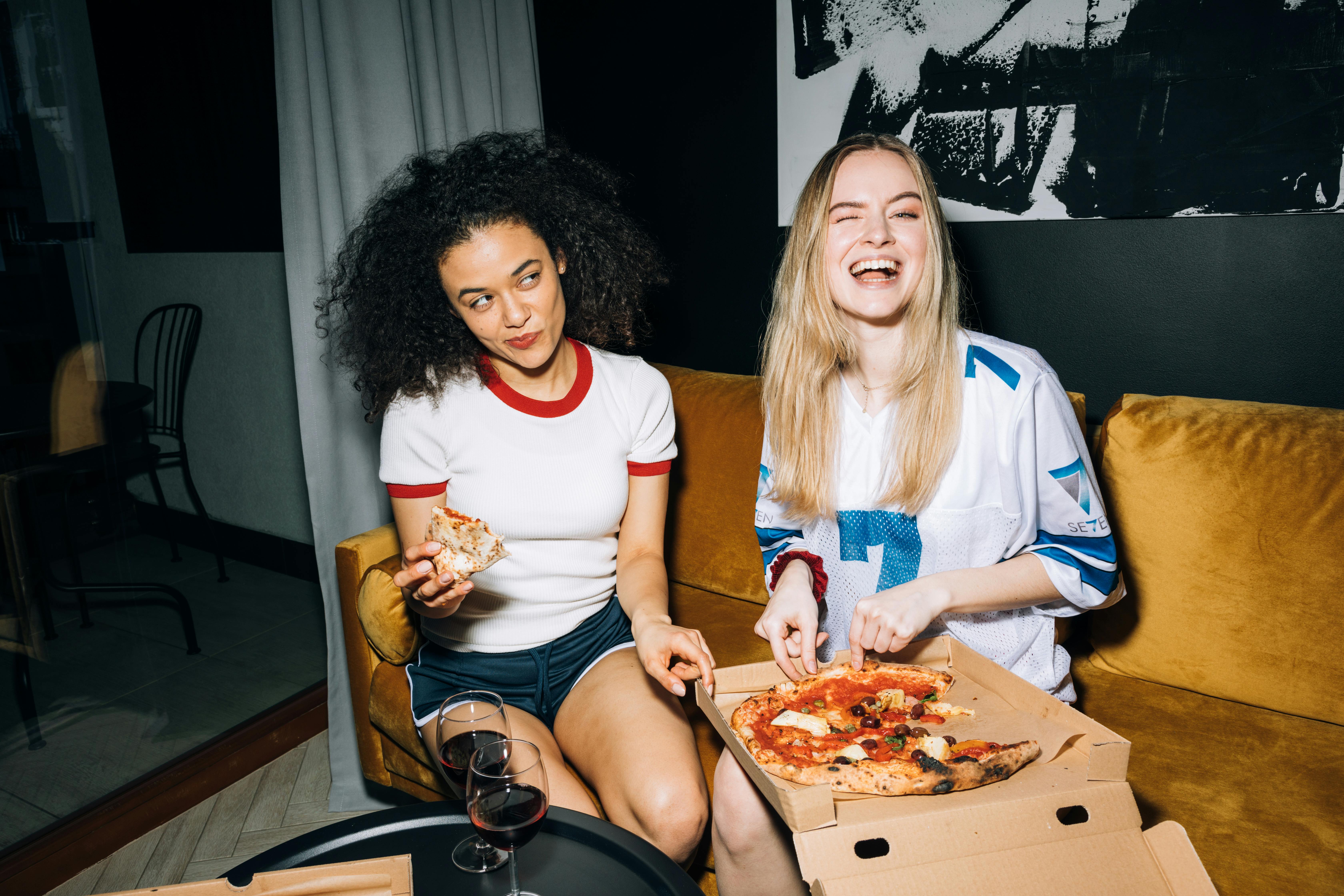 two young women eating and getting a slice of pizza