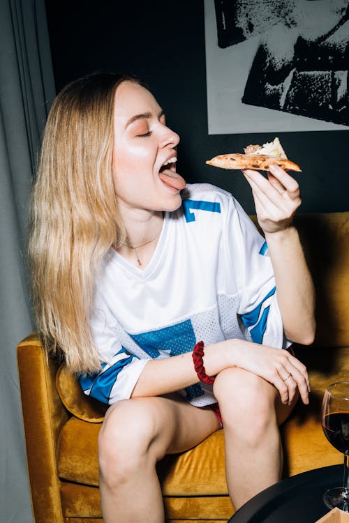 Young Woman Sitting on a Yellow Sofa While Eating Her Pizza