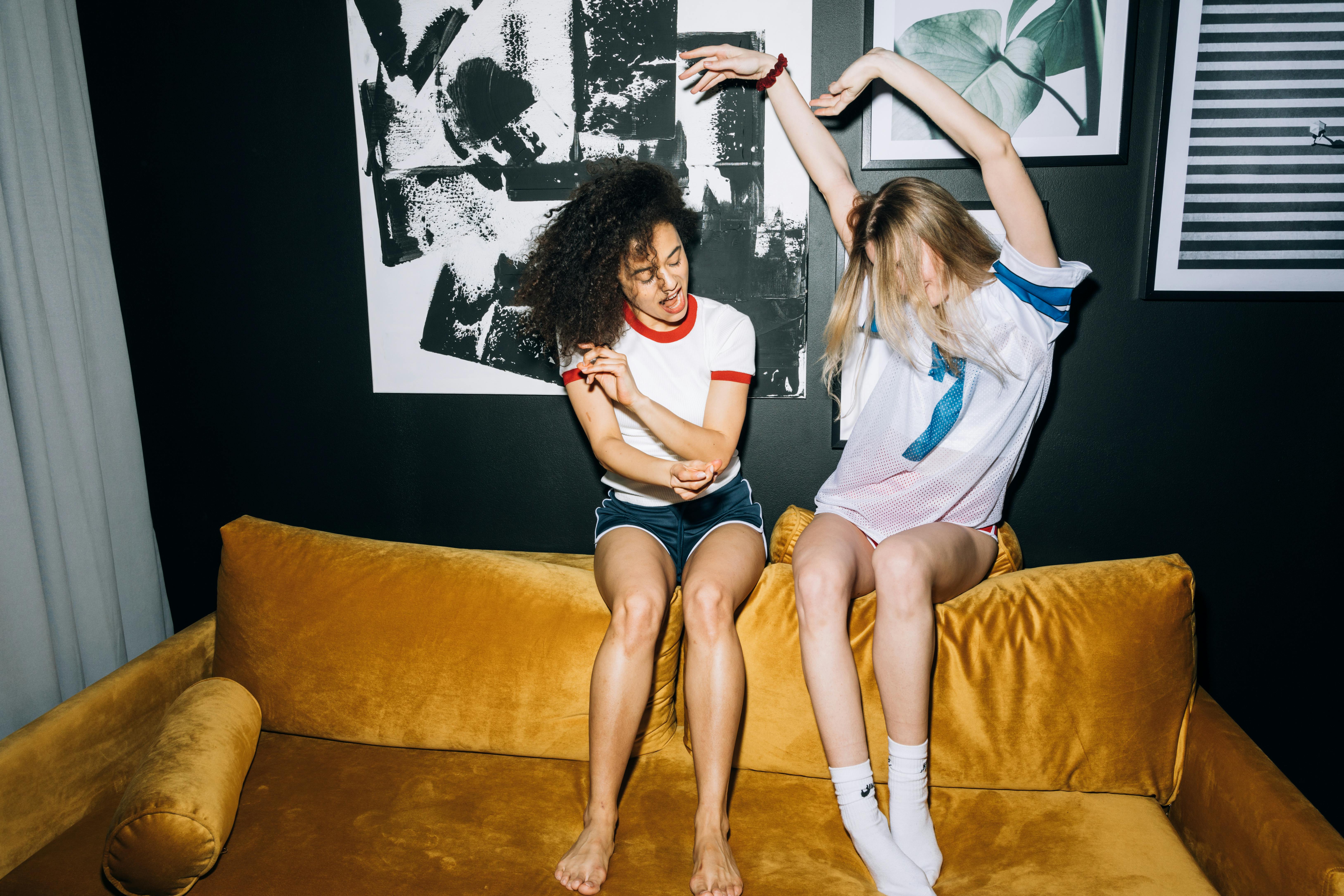 two young women having fun while sitting on a yellow sofa