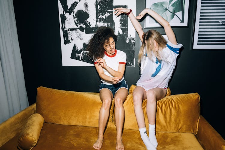 Two Young Women Having Fun While Sitting On A Yellow Sofa