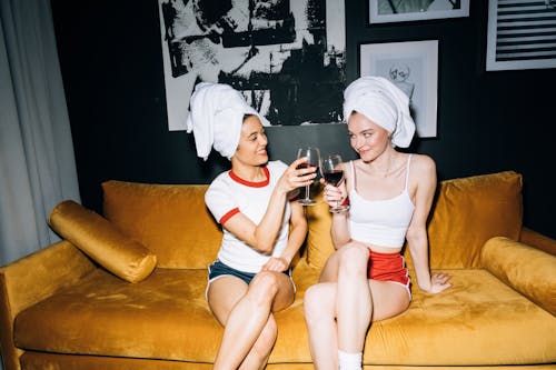 Two Young Women Sitting on a Yellow Sofa While Holding a Wine Glass With Red Wine