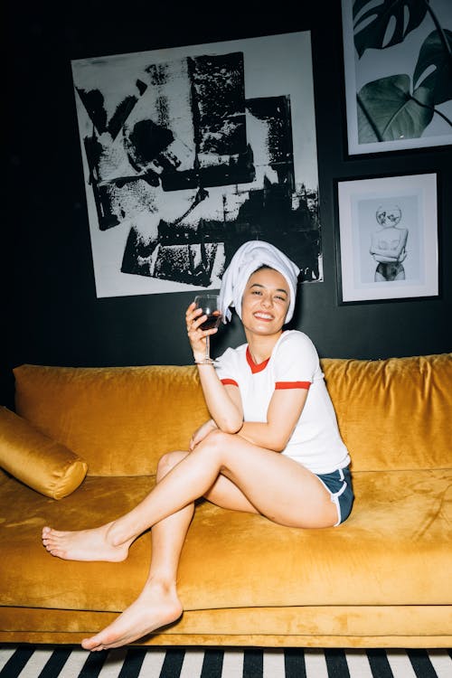 Young Woman Sitting on a Yellow Sofa While Holding a Wine Glass With Red Wine