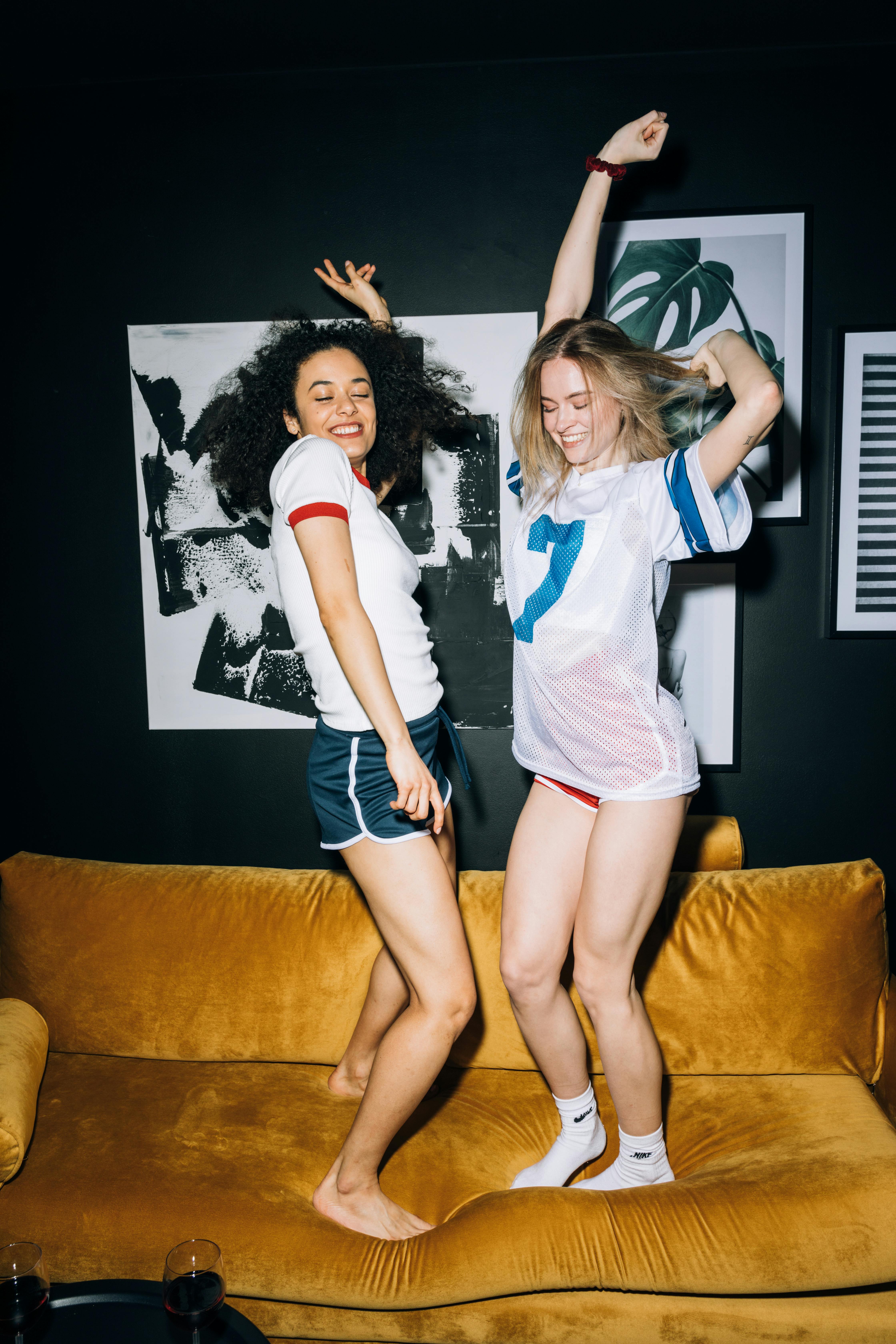 two young women having fun jumping on a yellow sofa