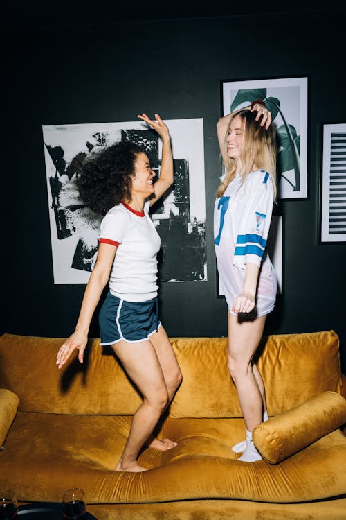 Free Two Young Women Having Fun Jumping on a Yellow Sofa Stock Photo