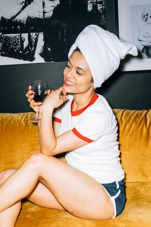 Young Woman Sitting on a Yellow Sofa While Holding a Wine Glass With Red Wine