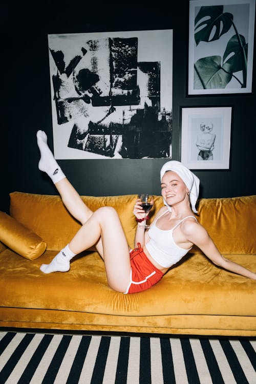 Young Woman Sitting on a Yellow Sofa While Holding a Wine Glass With Red Wine