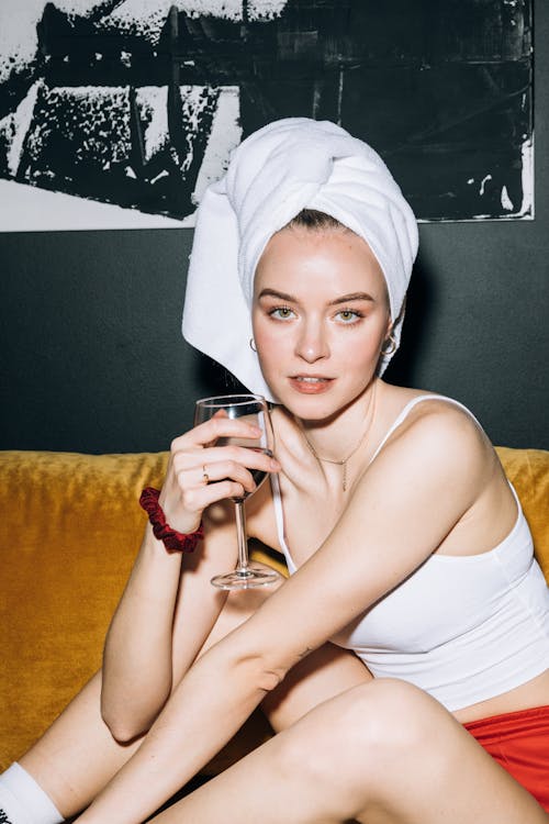 Young Woman Sitting on a Yellow Sofa While Holding a Wine Glass With Red Wine