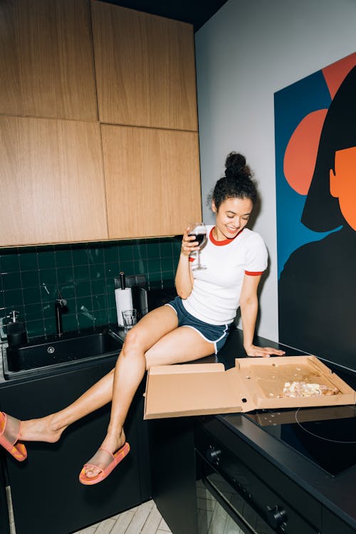 Young Woman Sitting on a Kitchen Counter While Looking at the Pizza