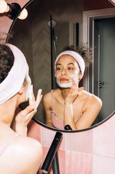 Young woman applying a face mask while looking in the mirror, enjoying her skincare routine.