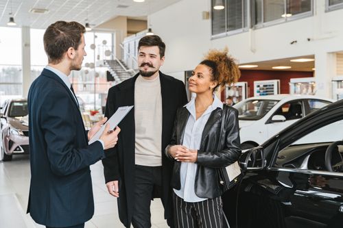 Free Couple discussing car purchase with salesman at indoor dealership, engaging conversation. Stock Photo