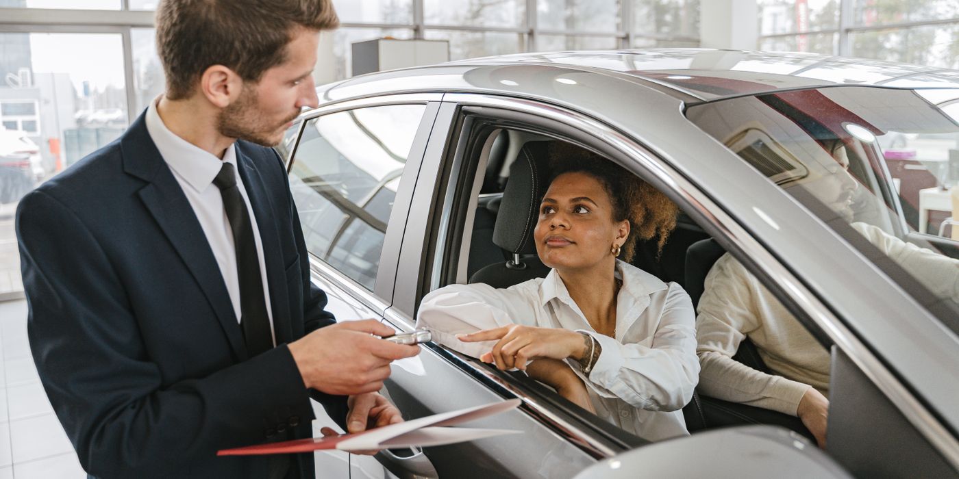 A salesperson going over paperwork with a new owner seated in her car at a dealership