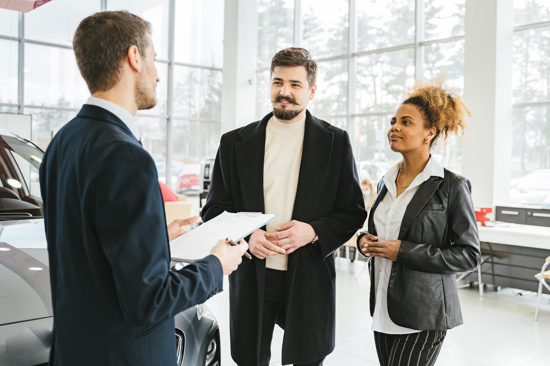 Happy couple discussing car purchase with dealer in showroom. Professional interaction and consultation.