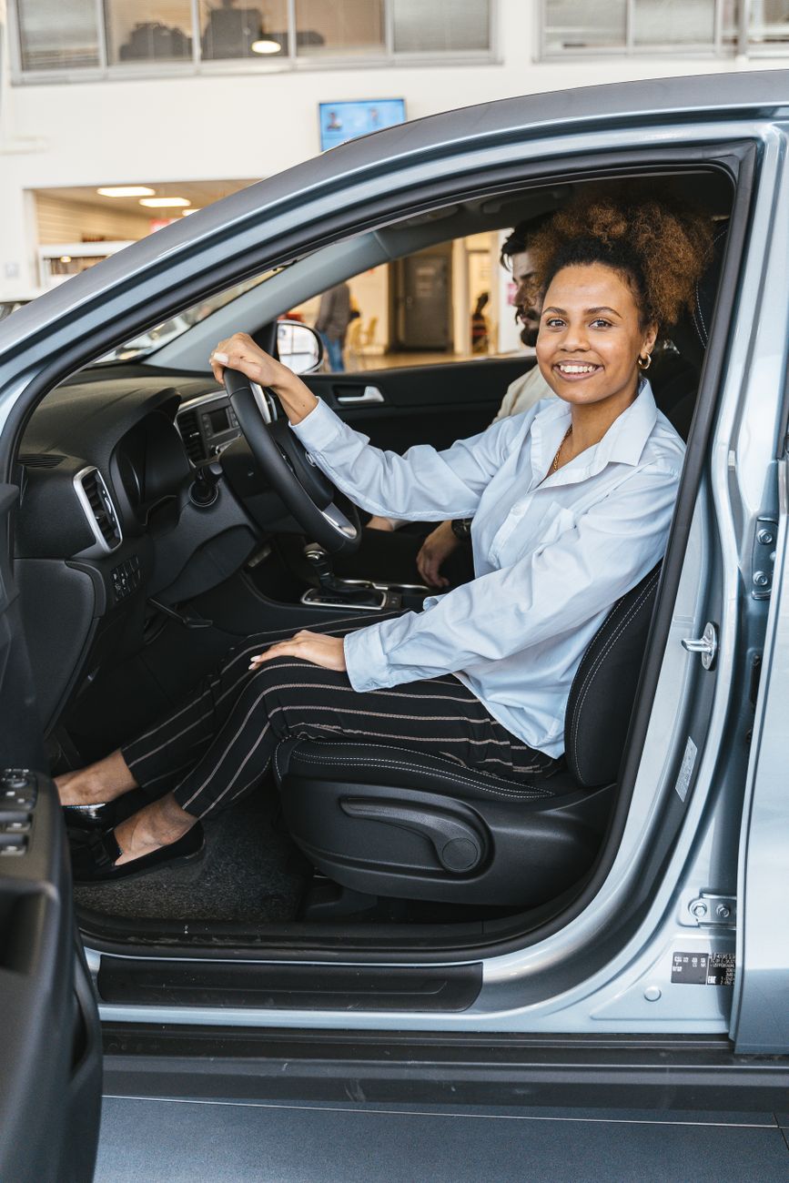 Smiling woman sitting in a car at a dealership, ready for a test drive