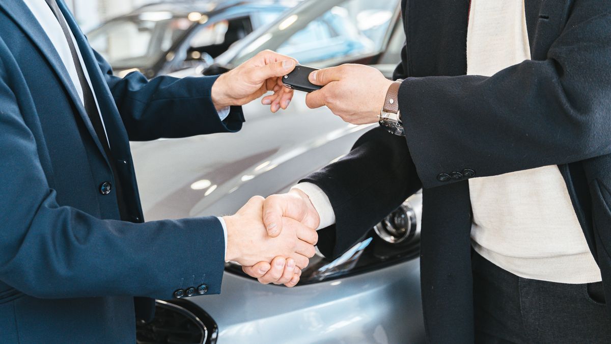 Two businessmen shaking hands and exchanging car keys in a dealership. Symbolizes a successful deal.