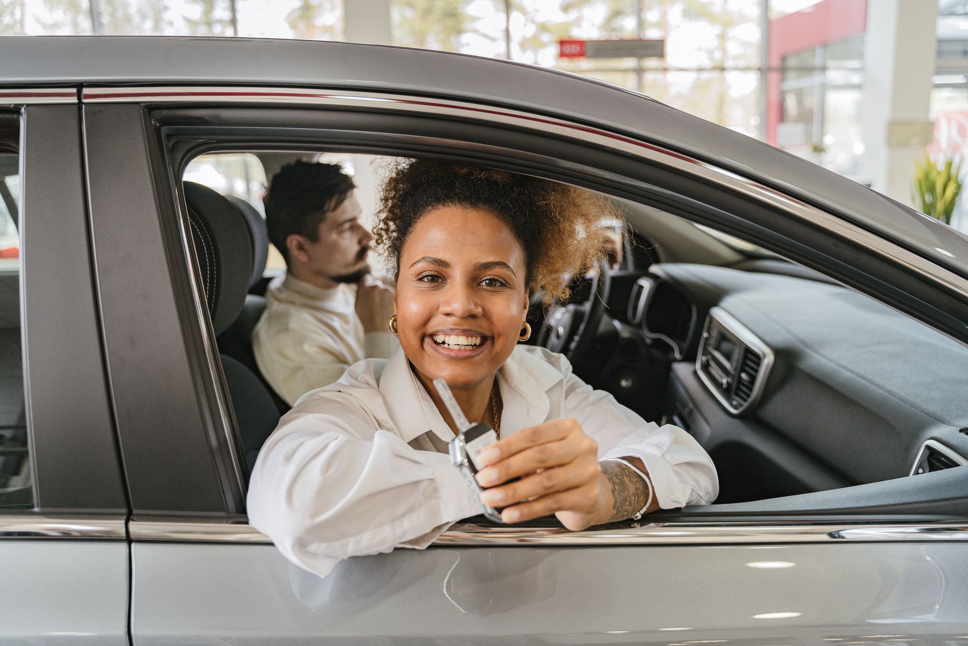 A couple sitting in their new car holding the keys inside a dealership showroom