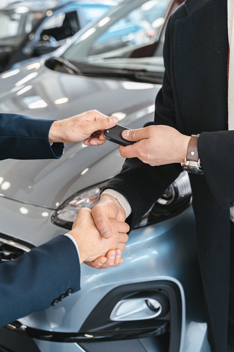 Close-up Of Men Shaking Hands And Handing In Keys To A New Car At The Car Salon 