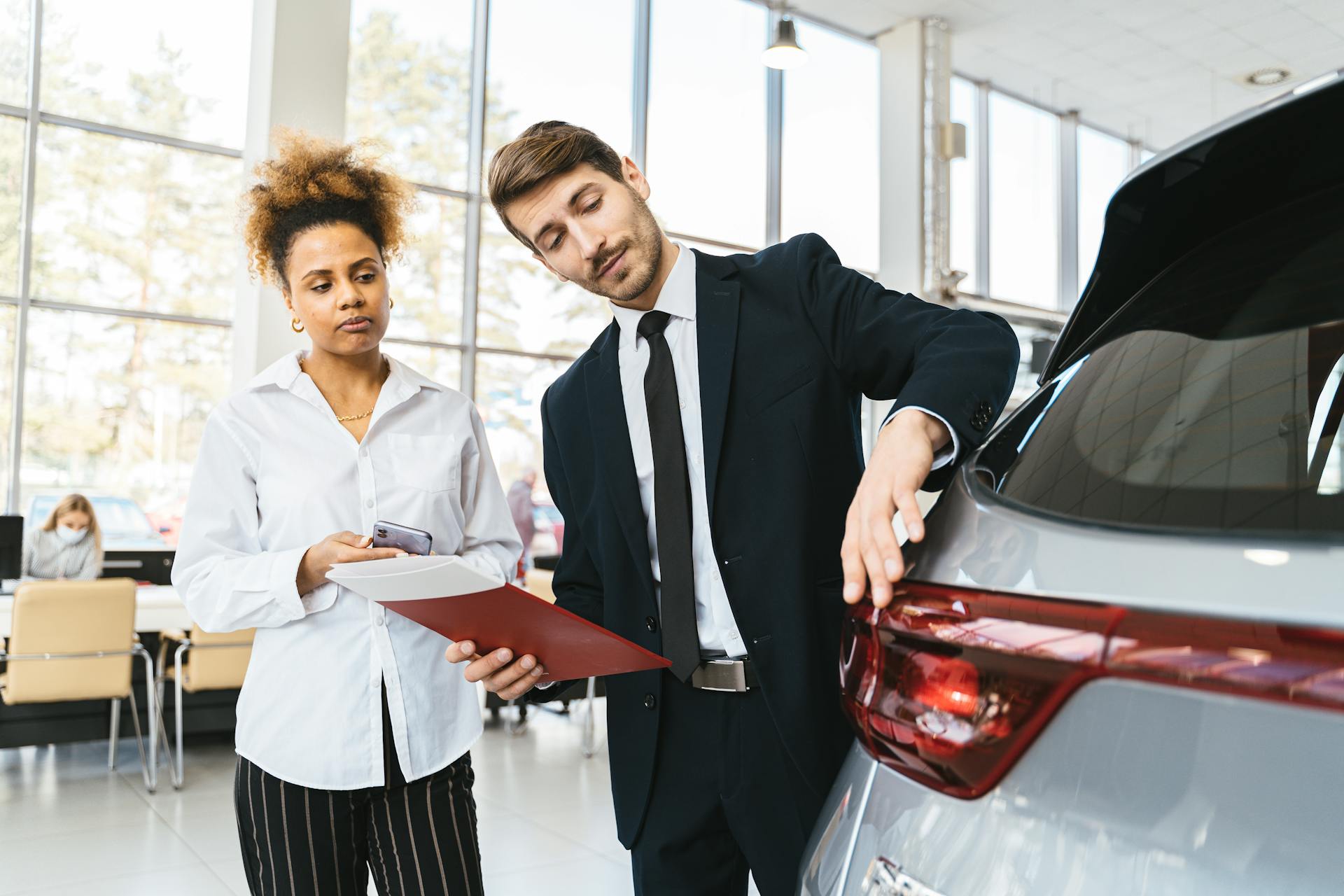 Businessman and customer discussing car purchase inside modern showroom.