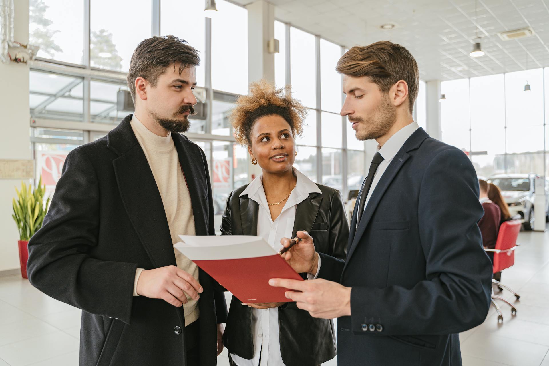 Business professionals discussing a car lease or purchase agreement in a showroom setting.