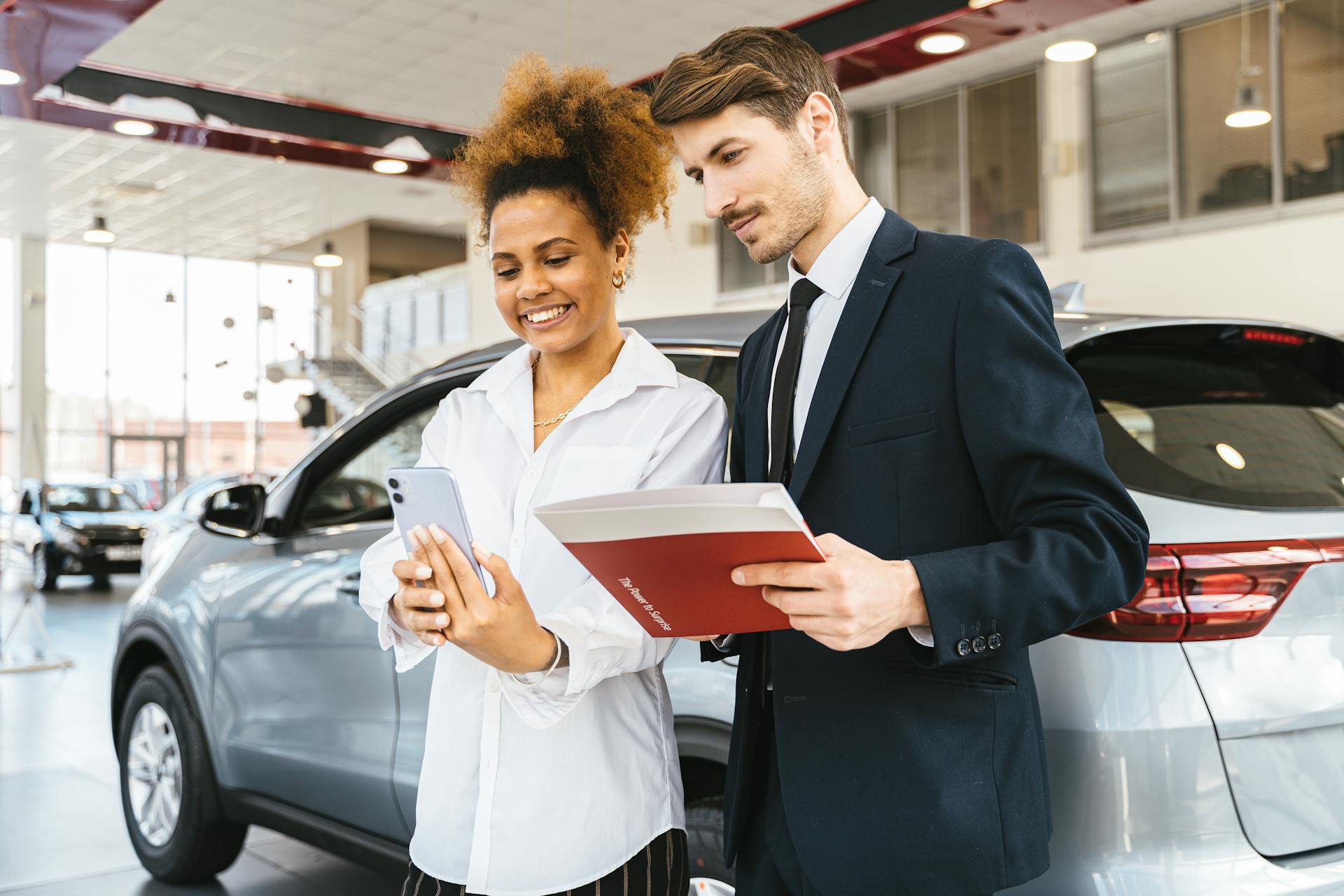 A woman and man smiling while reviewing details at a car dealership. Perfect for business or lifestyle imagery.