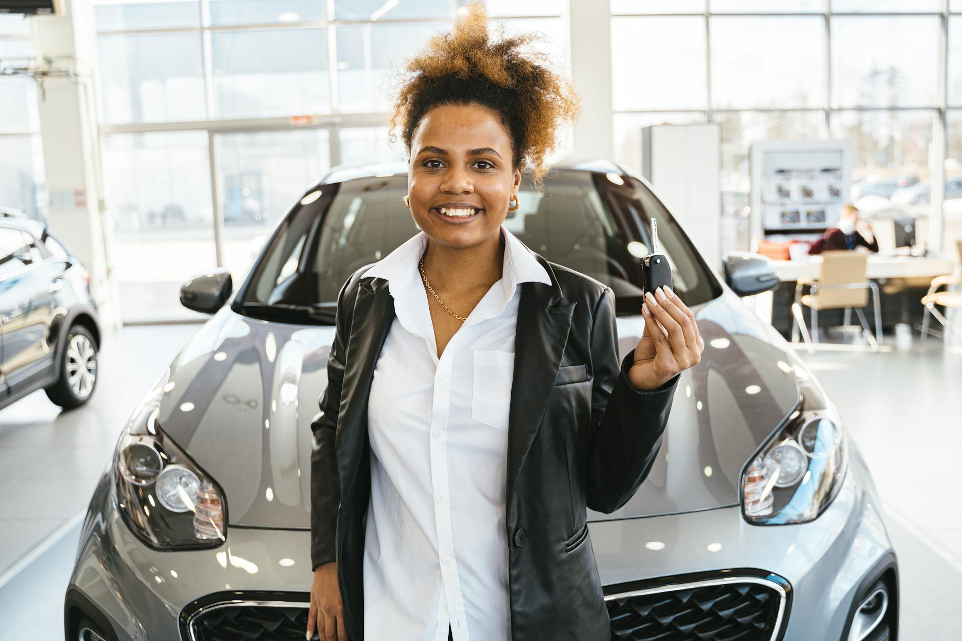 Smiling woman holding car keys in a dealership showroom, celebrating her new car purchase.