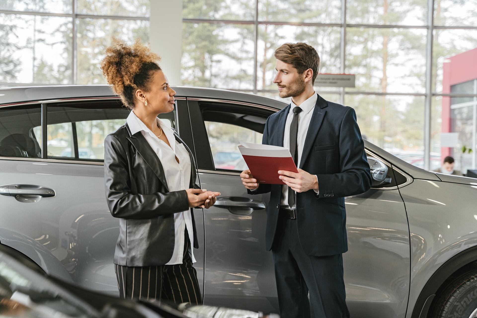 A woman discussing car purchase with a dealer inside a car dealership showroom.