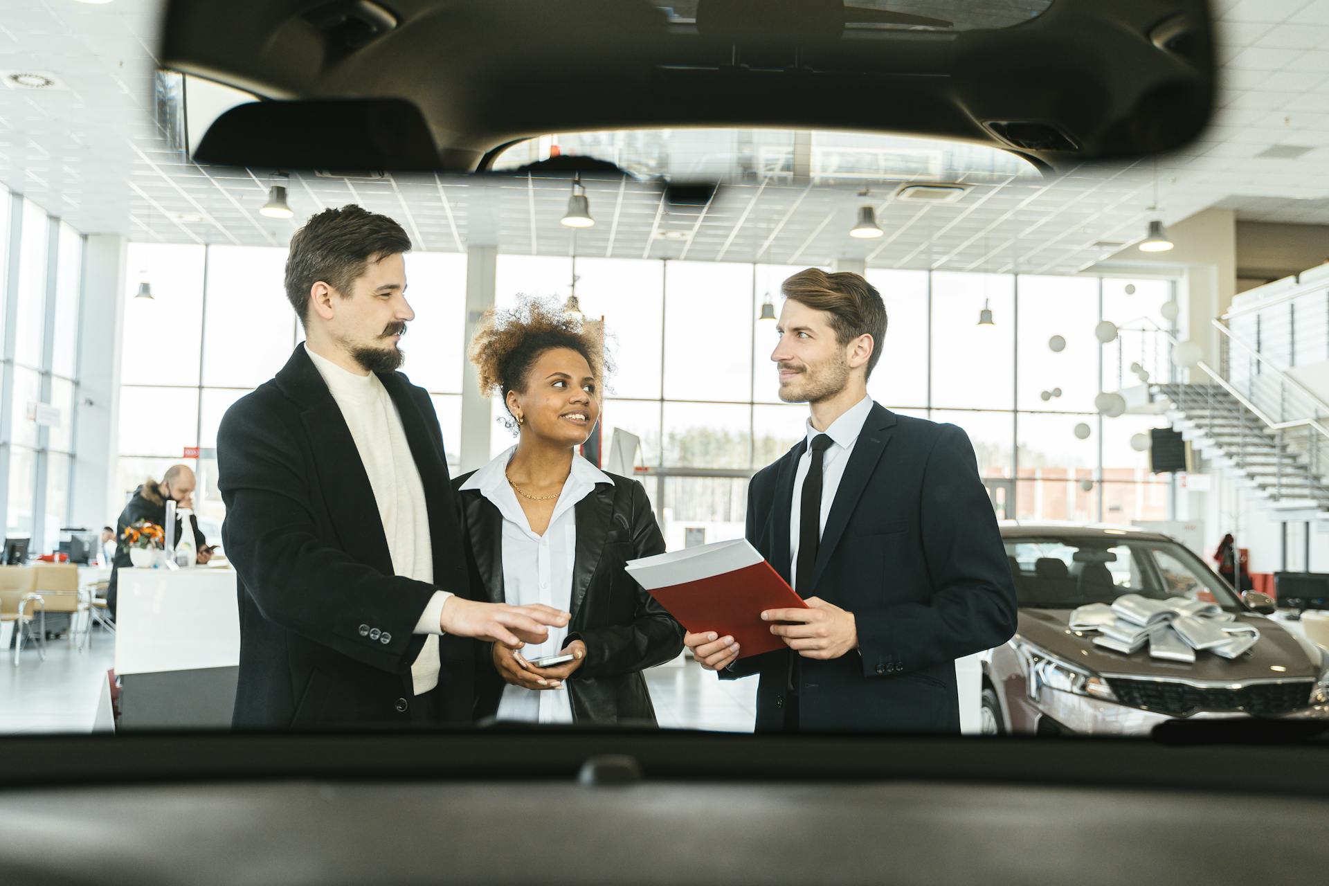 A diverse group of three people discussing car buying options indoors at a dealership.