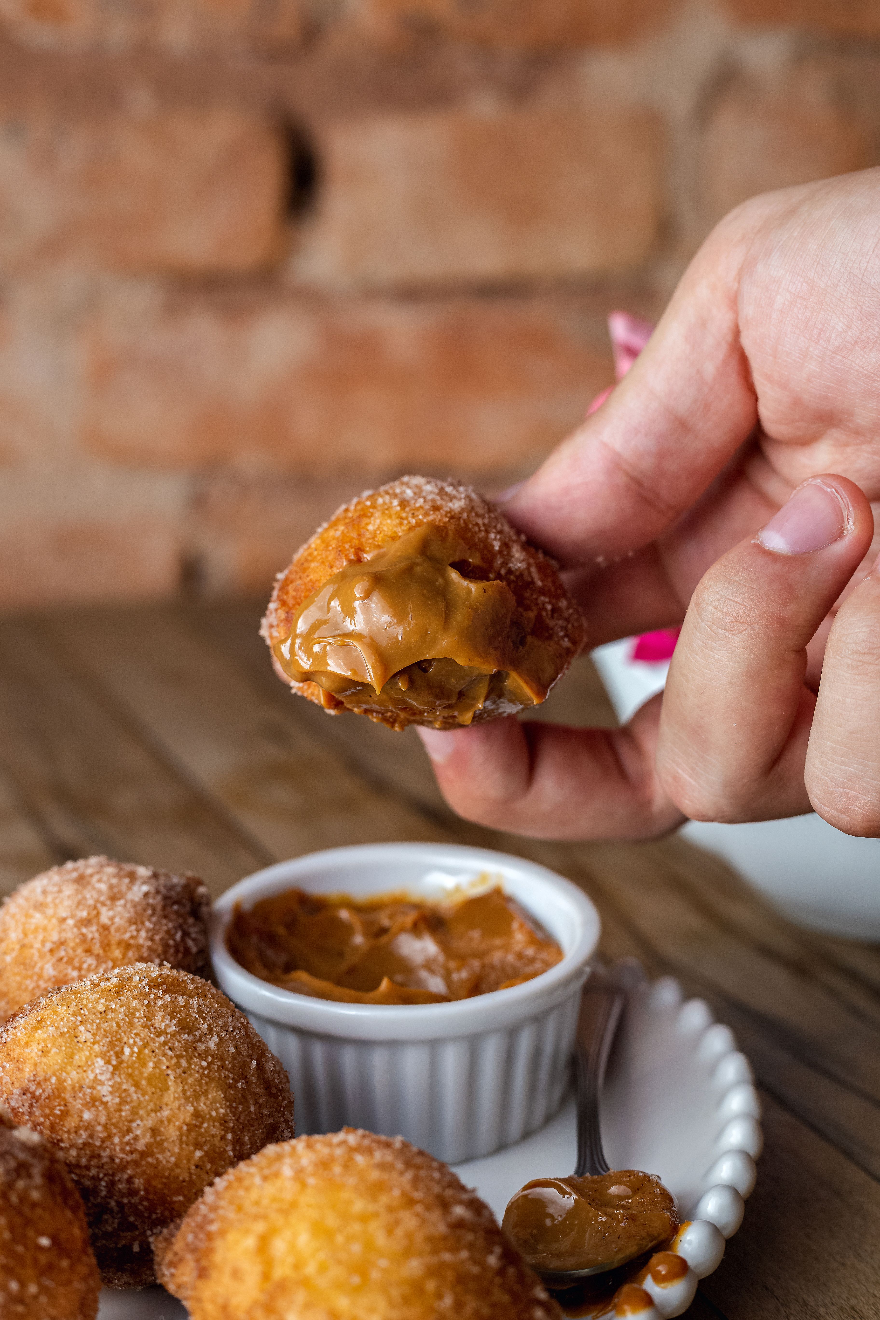 Close-up of a hand holding a caramel-filled mini donut, perfect for dessert lovers.