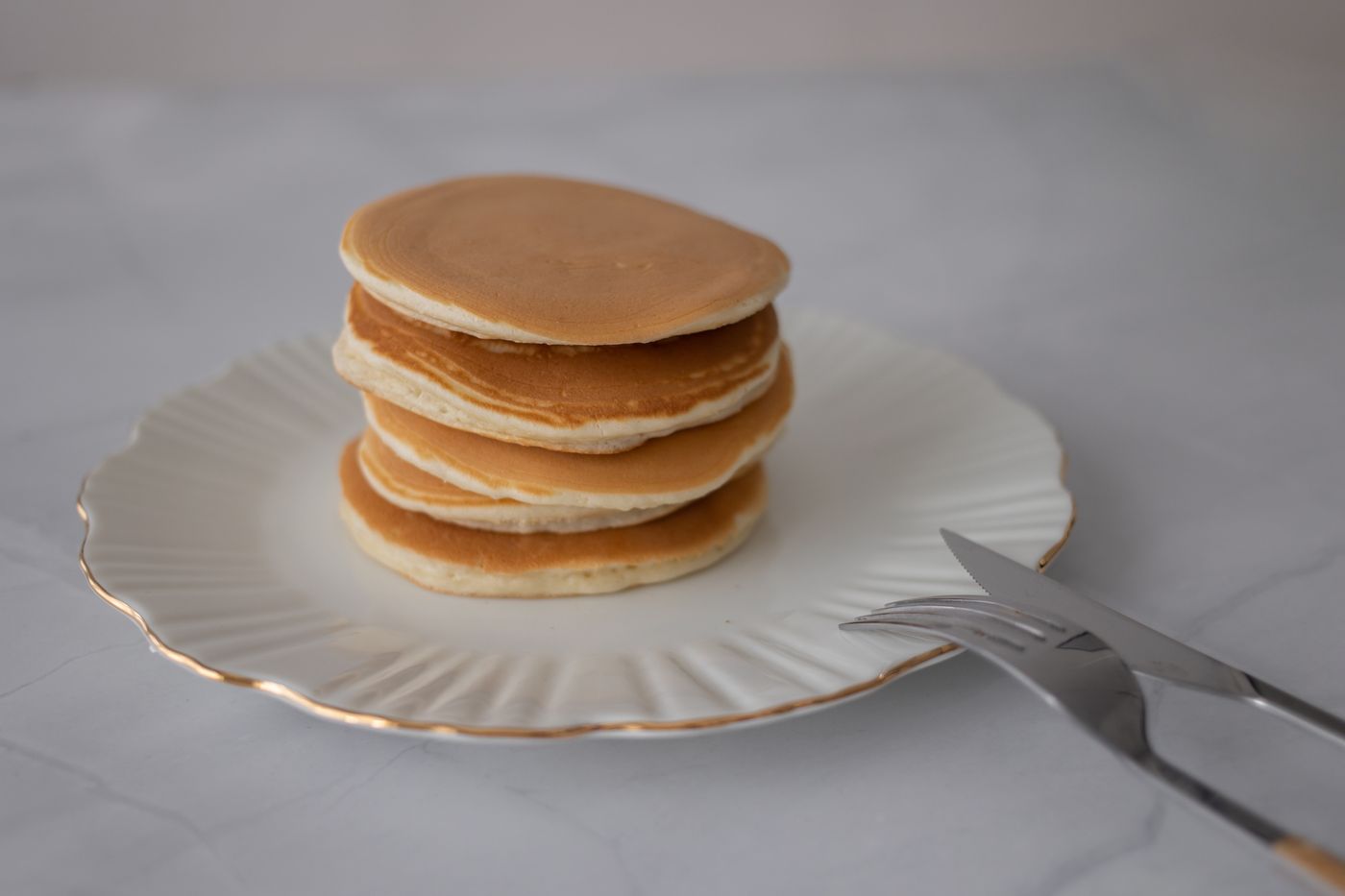 Stack of plain golden pancakes on a white plate showing their thickness
