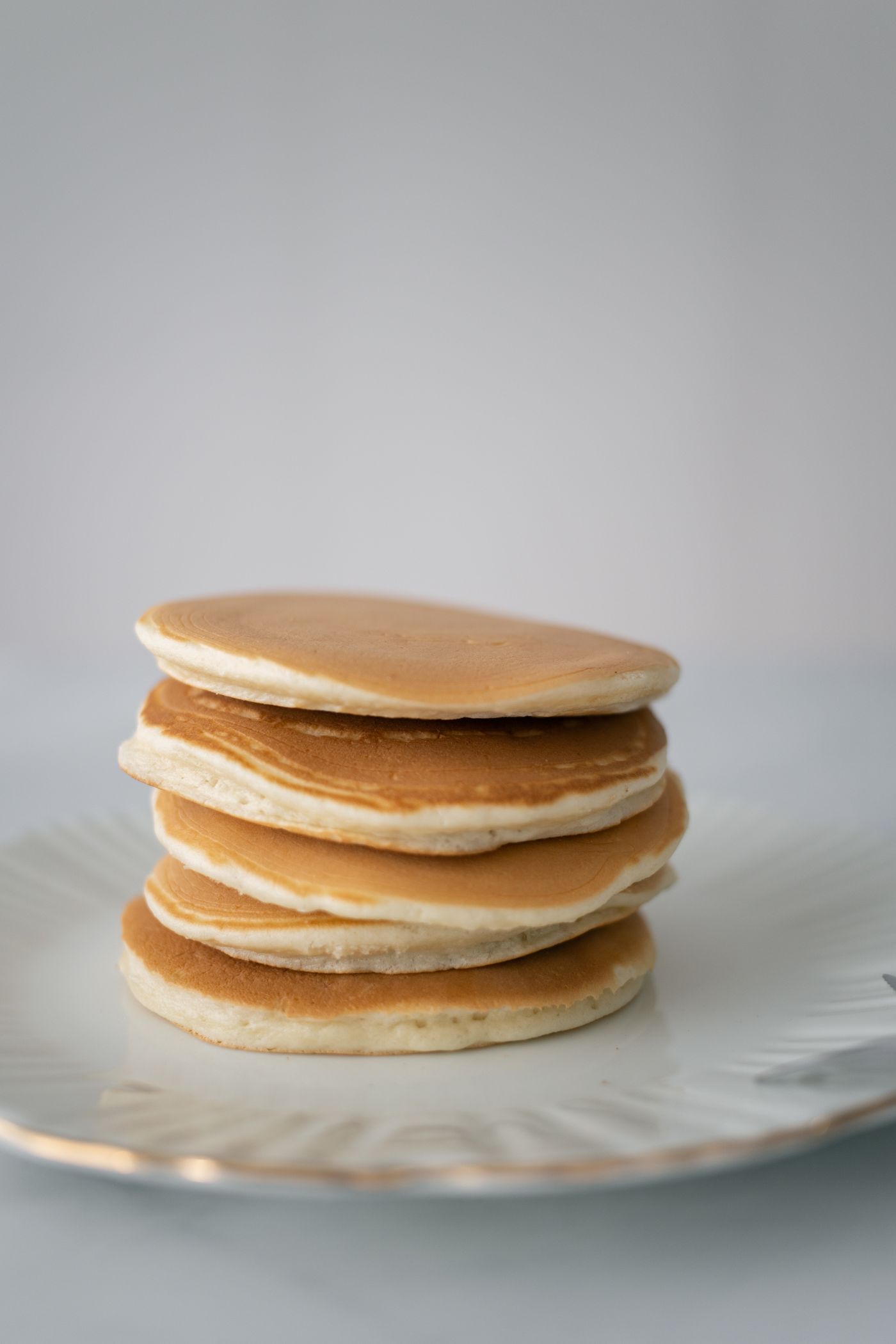 Tall stack of plain golden pancakes on a white plate