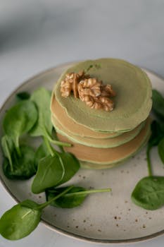 Artistic photo of a spinach pancake stack topped with walnuts on a plate.
