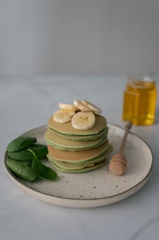 Delicious stack of spinach pancakes topped with bananas and honey, perfect for a healthy breakfast.