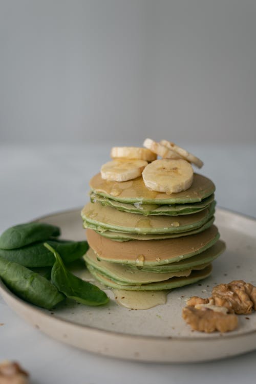 Tasty pancakes with syrup served on plate with fresh green leaves on white background