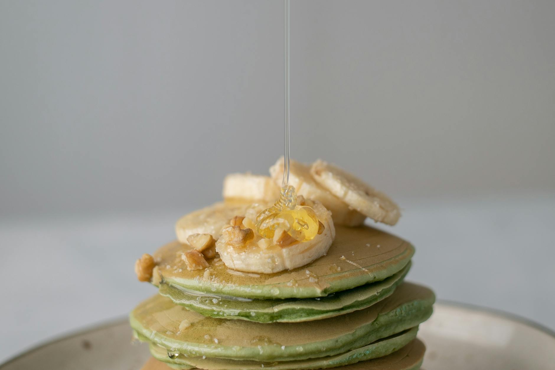 Appetizing sweet pancakes with honey and pieces of fresh banana on gray background