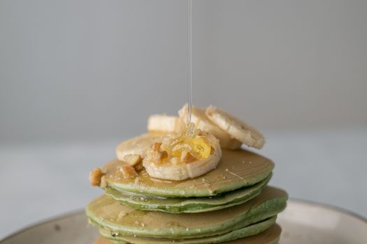 Appetizing sweet pancakes with honey and pieces of fresh banana on gray background