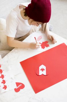 A child crafts a Canadian flag design using red paper indoors, celebrating creativity and national pride.