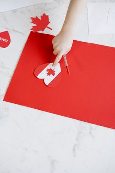 A child creating Canada-themed crafts with red paper cutouts, celebrating Canada Day.
