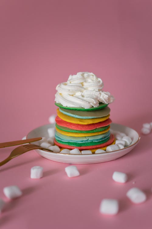 Free Stack of multicolored pancakes with whipped cream in pink studio Stock Photo