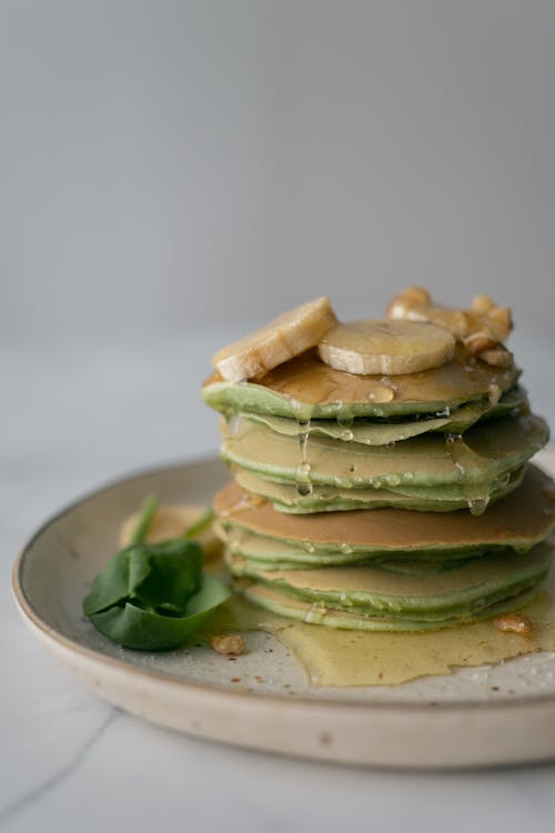 Free Stack of yummy healthy homemade pancakes stuffed with spinach and topped with syrup and sliced bananas on table Stock Photo