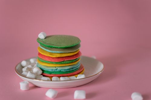 Free High angle of stack of multicolored appetizing pancakes stacked on plate with soft white marshmallows against pink background Stock Photo