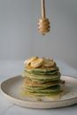 Person adding honey on pancakes with wooden dipper