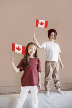 Two smiling children holding Canadian flags indoors, symbolizing patriotism and joy.