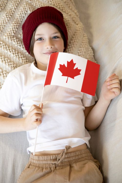 Free A smiling child lying down while holding a Canadian flag indoors. Stock Photo